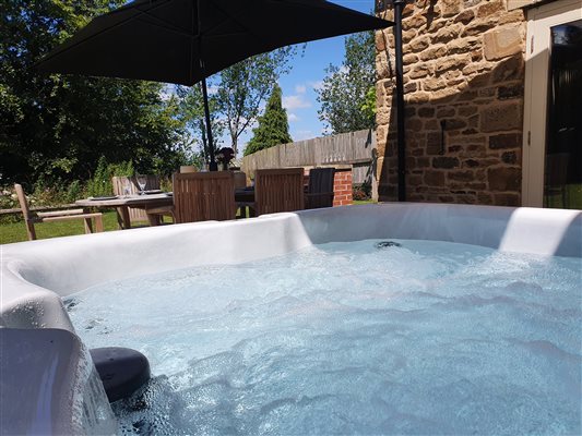 a close up of a bubbling hot tub with dappled sunlight reflecting off the surface, a large outdoor table with an open umbrella are in the background